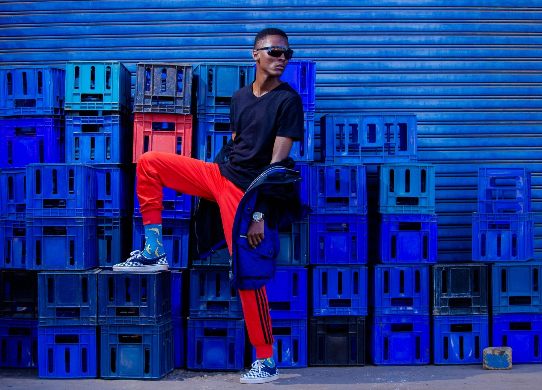 Stylish young man posing with vibrant streetwear against blue crates.